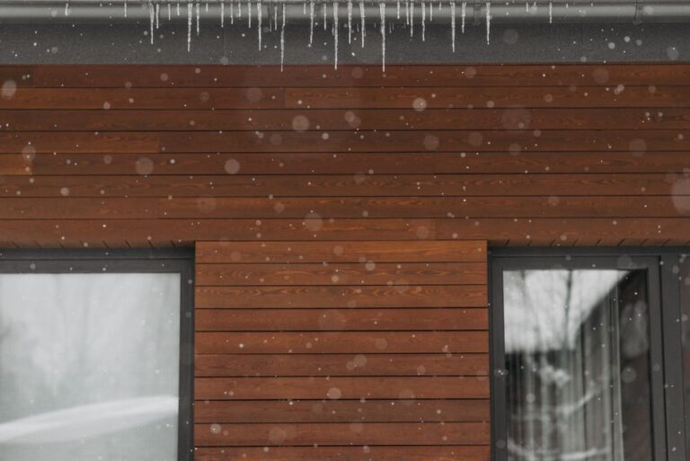 Close-up of a wooden wall with windows, adorned with icicles during a snowy winter day.