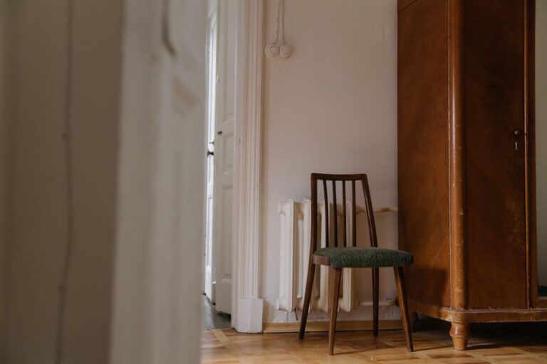 A cozy vintage room featuring a wooden chair and cabinet against a white wall.