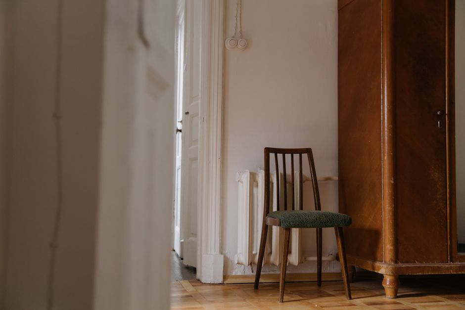A cozy vintage room featuring a wooden chair and cabinet against a white wall.