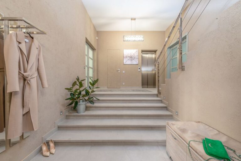 Modern lobby with elevator and wide staircase leading to hallway with bench and hanger shelf